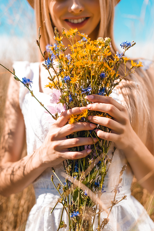 partial view of young woman holding bouquet of wildflowers, selective focus