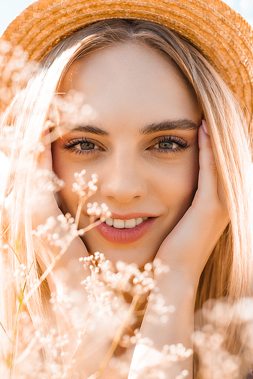 portrait of sensual blonde woman in straw hat  and touching face near wildflowers