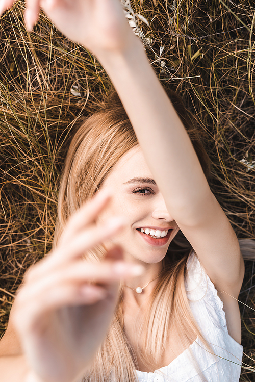 top view of excited blonde woman lying on grass with raised hands while , selective focus
