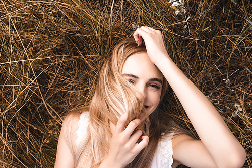 top view of young blonde woman lying on grass and  while obscuring face with hair
