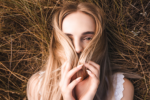 top view of young blonde woman obscuring face with hair while lying on grass and 