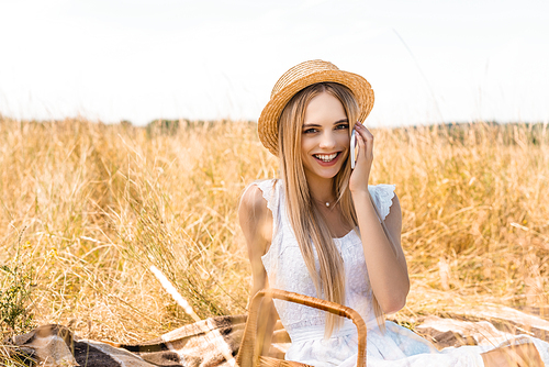 selective focus of stylish blonde woman in summer outfit talking on smartphone while  in field