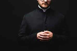 cropped view of priest with clenched hands isolated on black