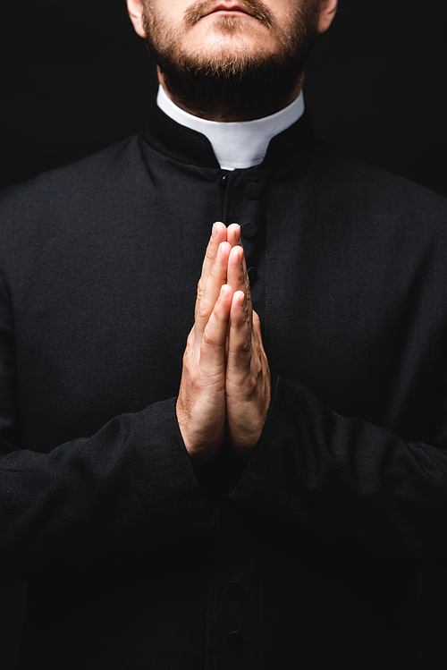 cropped view of priest with praying hands isolated on black