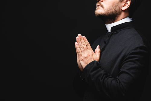 cropped view of bearded priest with praying hands isolated on black