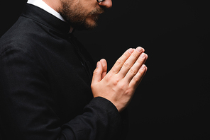 partial view of priest with praying hands isolated on black