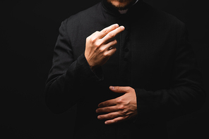 cropped view of priest gesturing while praying isolated on black