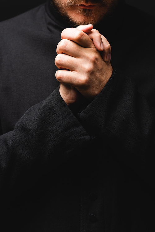 cropped view of priest with clenched hands praying isolated on black