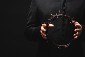 cropped view of pastor holding wreath with spikes in hands isolated on black