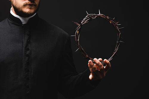 cropped view of pastor holding wreath with spikes in hand isolated on black