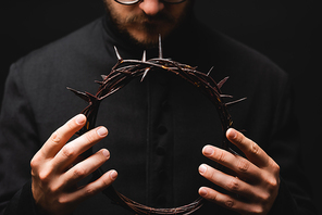 selective focus of priest holding wreath with spikes in hands isolated on black