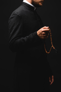 cropped view of priest holding rosary beads and standing isolated on black