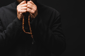 cropped view of priest holding rosary beads in hands and praying isolated on black
