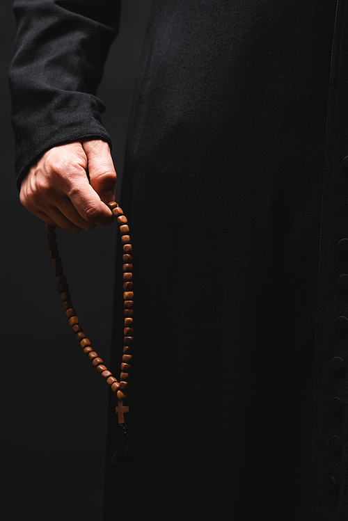 partial view of pastor holding rosary beads in hand isolated on black