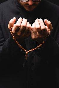 cropped view of pastor holding rosary beads in hands and praying isolated on black