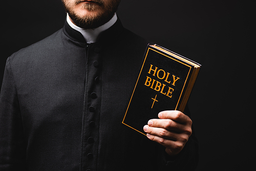 cropped view of priest holding holy bible isolated on black