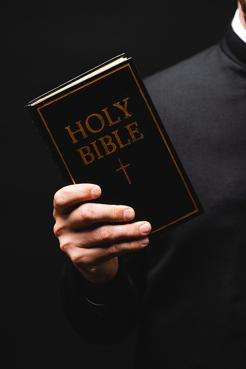 cropped view of priest holding holy bible in hand isolated on black