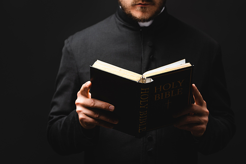 partial view of bearded pastor reading holy bible isolated on black