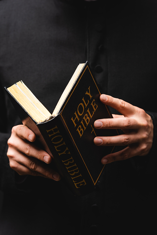 partial view of pastor reading holy bible isolated on black