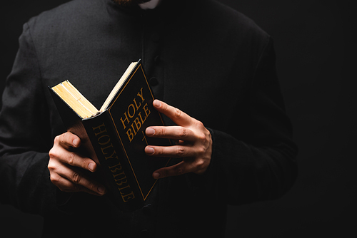 partial view of pastor holding holy bible in hands isolated on black