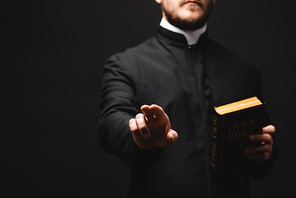 selective focus of priest holding holy bible while gesturing isolated on black