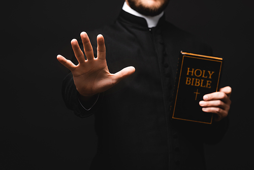 cropped view of priest holding holy bible while gesturing isolated on black