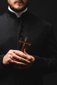 cropped view of bearded priest holding wooden cross isolated on black