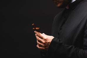 cropped view of priest holding cross isolated on black