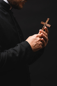 cropped view of priest holding wooden cross isolated on black
