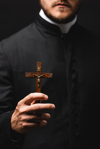 selective focus of priest holding wooden cross isolated on black