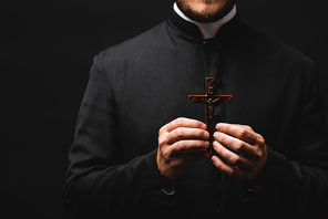 cropped view of pastor holding wooden cross isolated on black