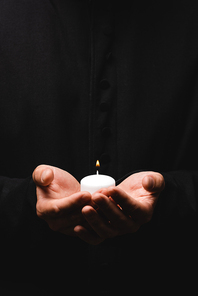 cropped view of pastor holding burning candle isolated on black