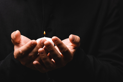 partial view of priest holding burning candle isolated on black
