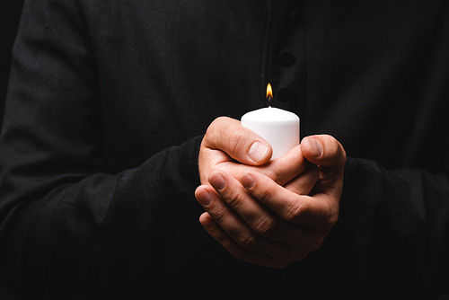 cropped view of priest holding burning candle in hands isolated on black