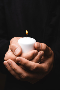 cropped view of priest holding burning candle isolated on black