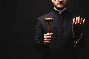 cropped view of bearded priest holding wooden gavel and rosary beads isolated on black