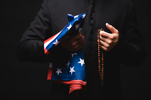 cropped view of priest holding american flag and rosary beads in hands isolated on black