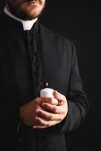 cropped view of bearded priest holding burning candle in hands isolated on black