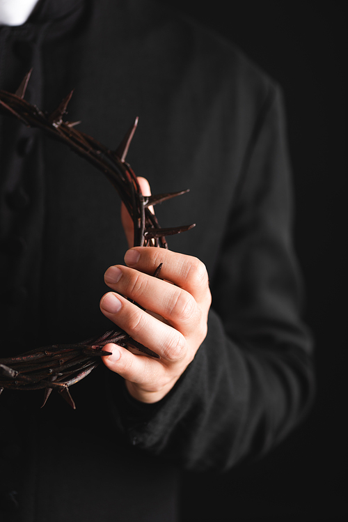 selective focus of priest holding sharp wreath with spikes isolated on black