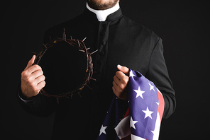 cropped view of priest holding wreath with spikes and american flag isolated on black