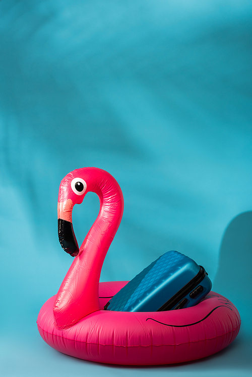 pink inflatable flamingo and suitcase on blue background