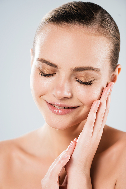 cheerful young woman touching face isolated on grey