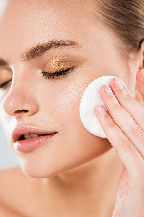 close up of young woman holding cotton pad near face isolated on grey