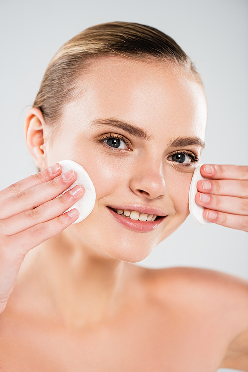 happy young woman holding cotton pads near clean face isolated on grey