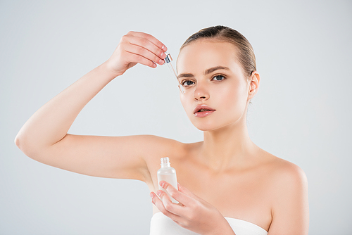 attractive woman holding bottle and applying serum isolated on grey