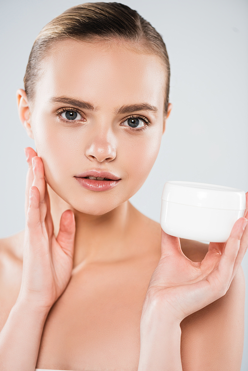 pretty woman holding container with face cream and touching clean face isolated on grey