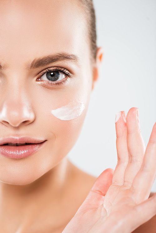 cropped view of young woman applying face cream isolated on grey