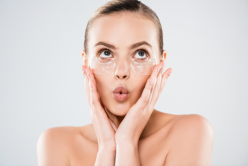 surprised woman touching face and eye patches isolated on grey