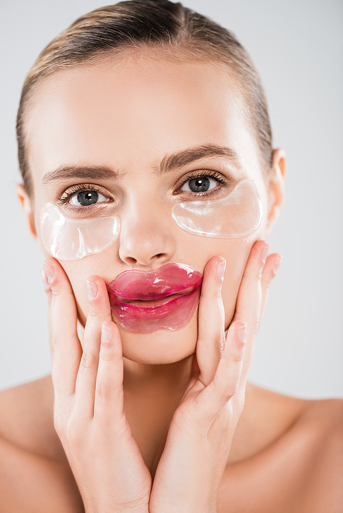 beautiful woman with lip mask and eye patches touching clean face isolated on grey