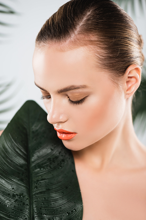 attractive woman with makeup looking at green leaf on white